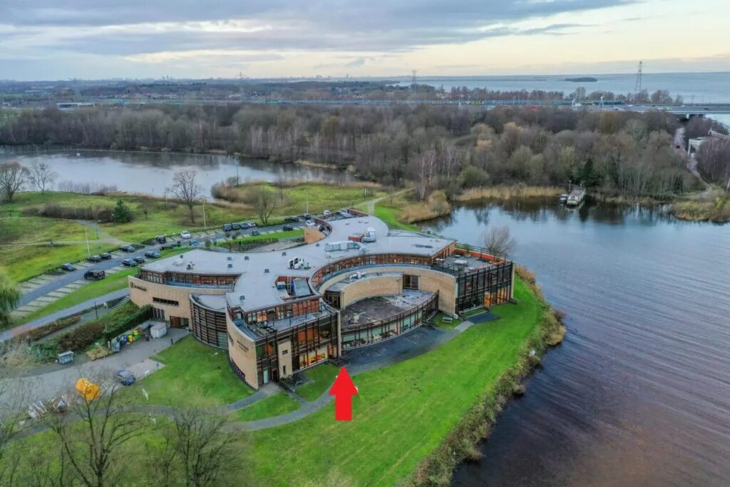 Luchtfoto van het Waterschapshuis met een rode pijl die een specifieke ingang aan de waterzijde markeert.