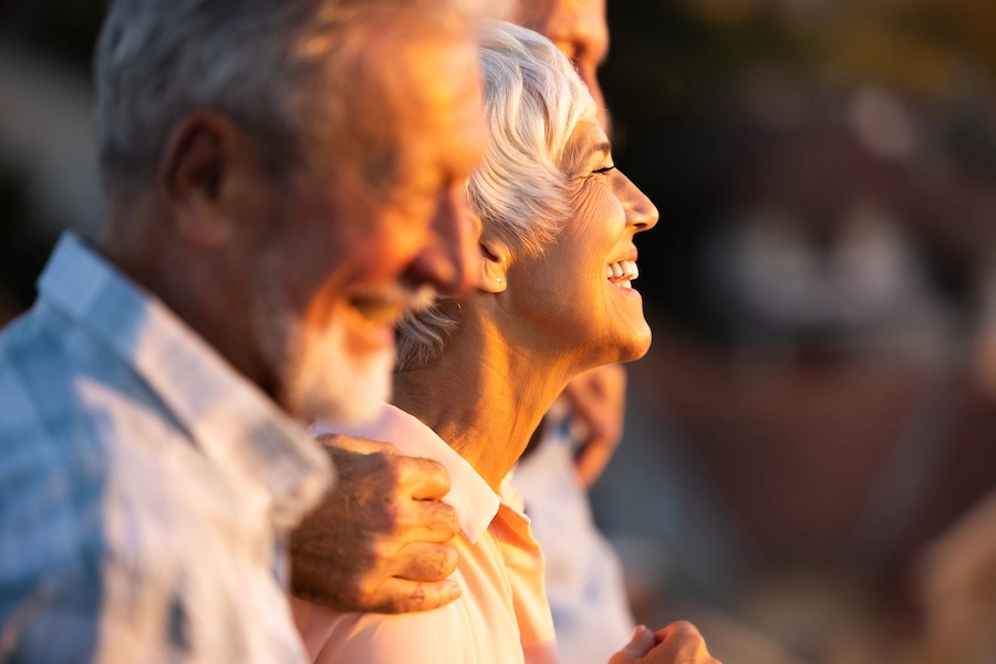 Drie lachende oudere mensen genieten samen van het warme zonlicht in een gouden gloed.