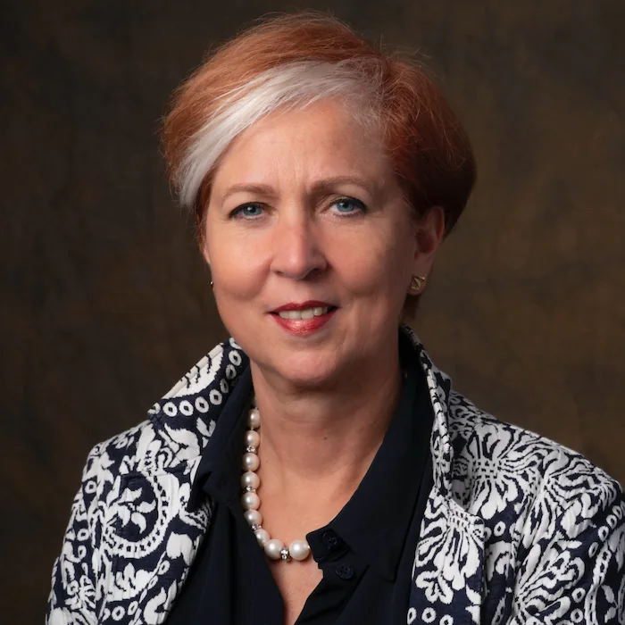Portret van Ellen Botman met korte rood-witte haren, een parelketting en een donkerblauw-wit patroonvest.